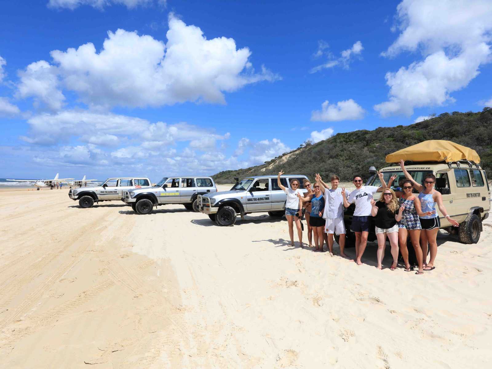 Group of backpackers posing in front of a Hard Tag-Along Tour convoy of 4WD