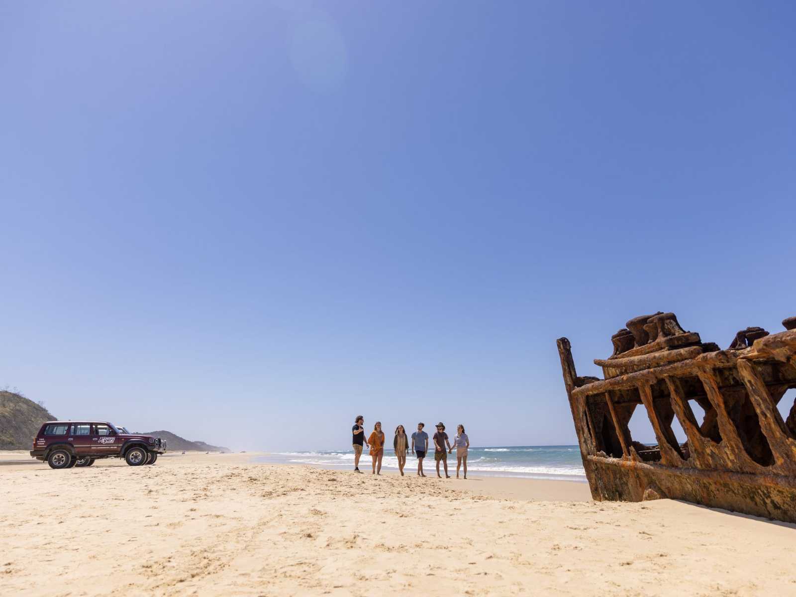 Backpackers walking along 75 Mile Beach past the Maheno Shipwreck on K'gari